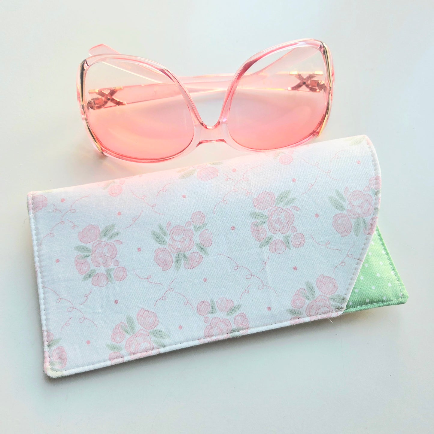 Pink sunglasses on a floral-patterned case against a light background