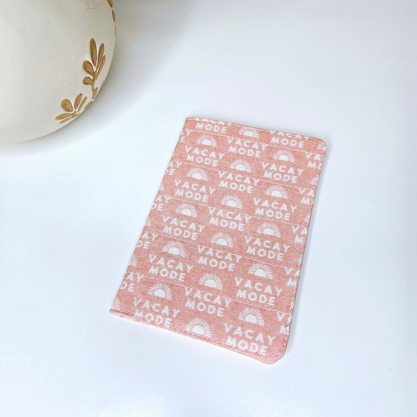 A passport cover with a 'VACAY-MODE' text and geometric patterns in pink