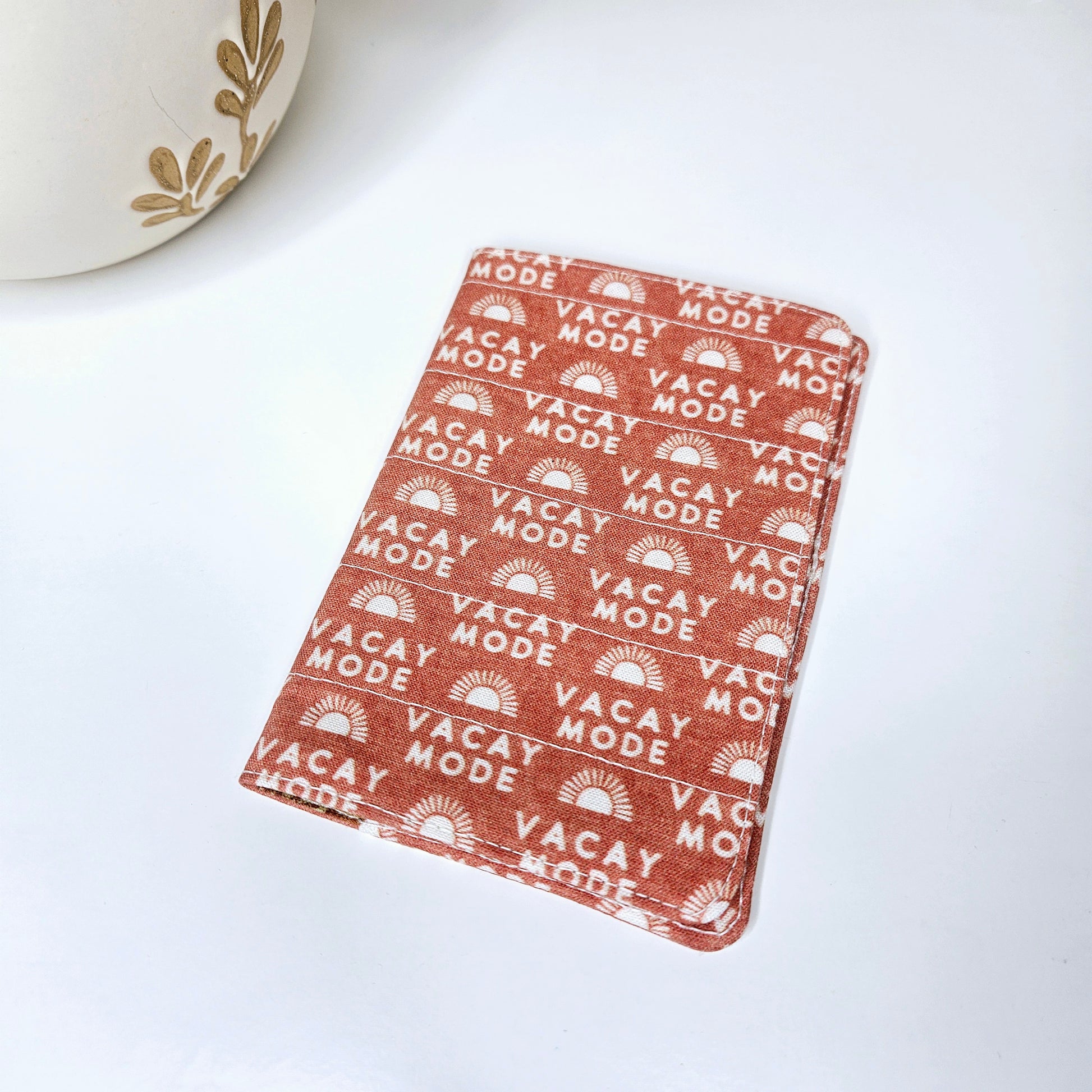 A passport cover with a 'VACAY-MODE' text and geometric patterns in red brick