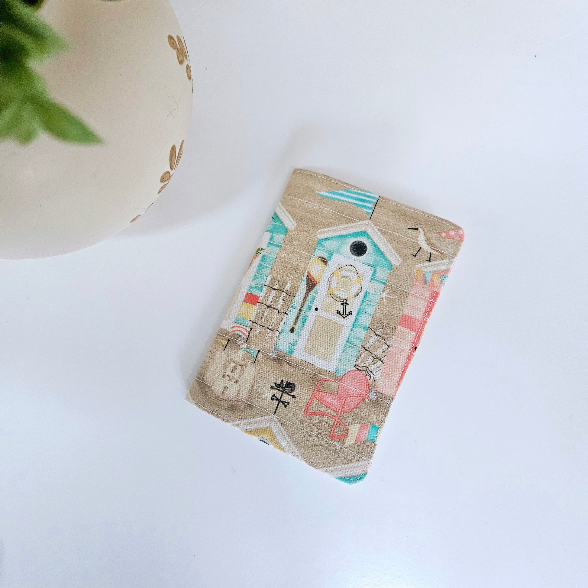 A multicolored passport cover with a beach theme, featuring illustrations of beach houses, boats, and people.
