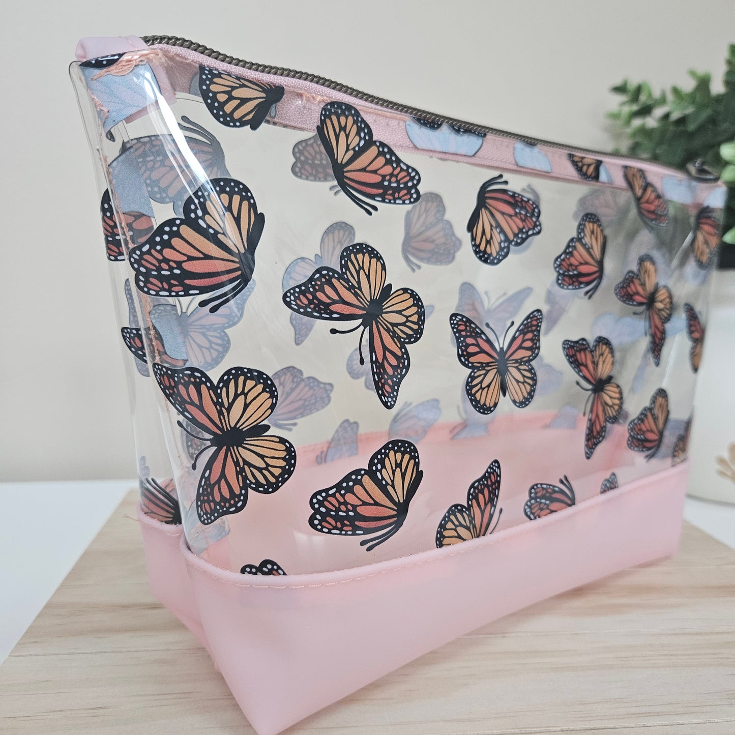 A clear TPU vinyl travel pouch with a butterfly print design, featuring a solid pink base.
