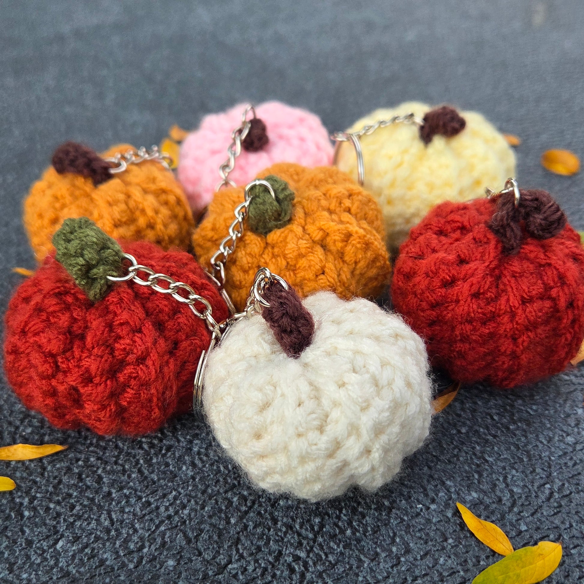 Crochet pumpkin keychain styled with autumn leaves and cozy fall decor as a seasonal gift idea.