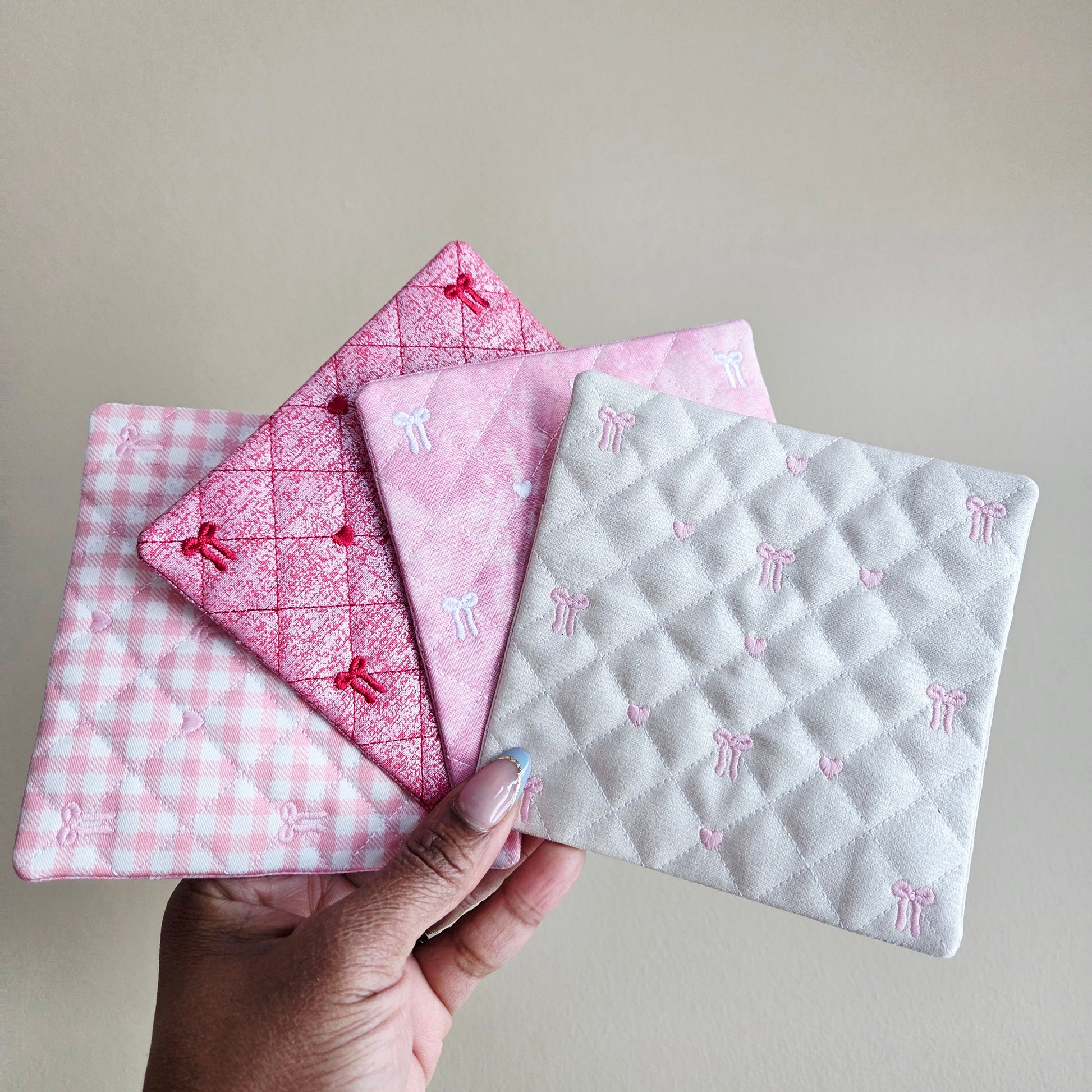 Hand holding three pink and white patterned fabric pieces against a neutral background